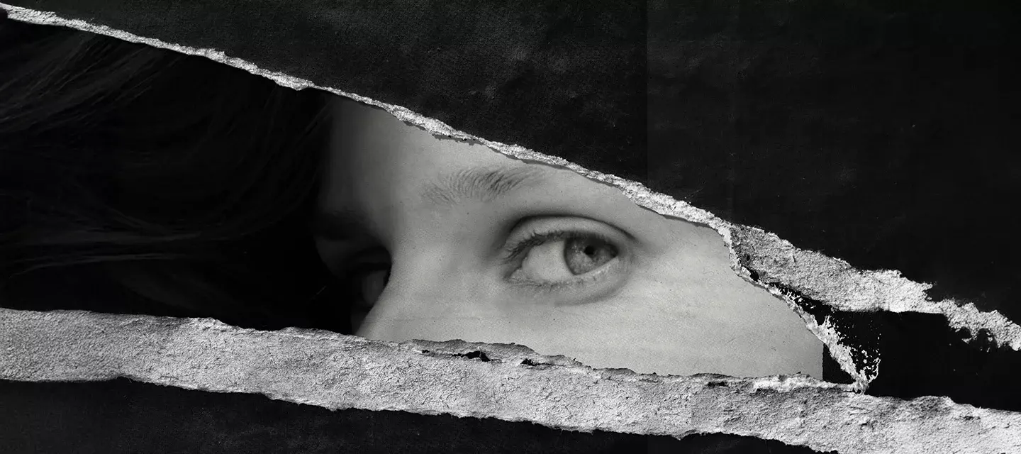 A torn up black and wihte poster on the wall where only a womans eyes remain, looking at the viewer